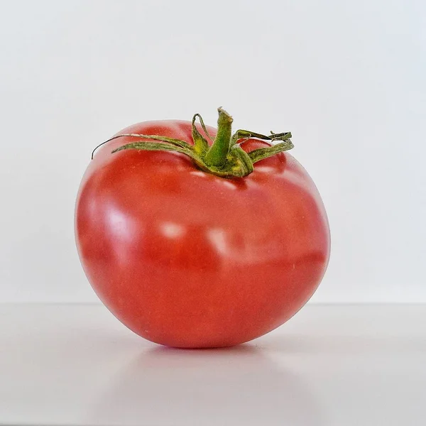 Um tomate vermelho sentado em uma mesa branca — Fotografia de Stock