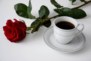 Kırmızı gül, bir fincan kahve tabakta, gri çay seti beyaz masada.