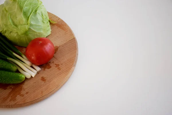 Lahana, salatalık, domates, yeşil soğan, beyaz arka planda tahta kesme tahtasında salata.
