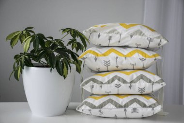 Dört dekoratif yastık gri ve sarı renkte. Evin yanında beyaz saksıda bitki var.