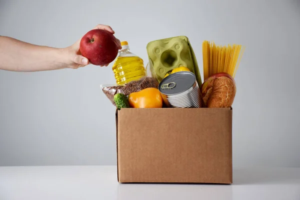 Gönüllü, içinde sebzeler, meyveler, yumurtalar, konserve yiyecekler, spagetti ve yağ bulunan bağış kartonları paketliyor. İnternetten market alışverişi, bağış veya teslimat hizmeti kavramı.
