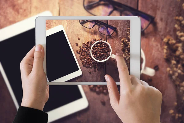 Hand girl hoding ipad take photo of cup of coffee on wood table — Stock Photo, Image