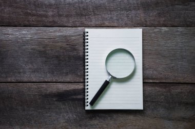 Not defteri ve ahşap masa üzerinde büyüteç