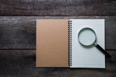 Not defteri ve ahşap masa üzerinde büyüteç