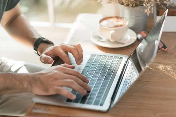 Zblízka ruky muž pracuje s notebookem a pít horkou kávu v kavárně — Stock fotografie