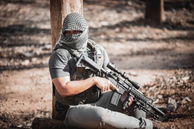 Terörist adam maske takıyor ve elinde silah tutuyor.