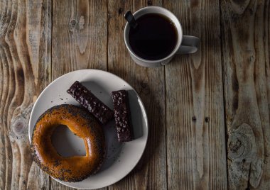 Kahvaltıda haşhaşlı simit ve çikolatalı waffle. Tahta masada bir kupa sıcak çayla birlikte beyaz bir tabakta.