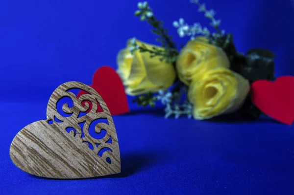 heart made of wood on a blue background with a yellow bouquet of flowers