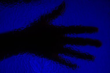 Mavi arka planda desenleri olan bir camın arkasında bir elin gölgesi