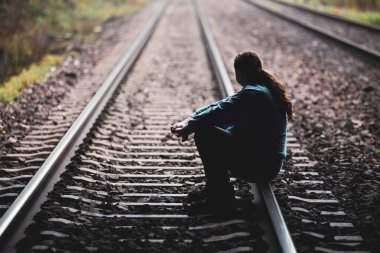 Young man sitting on the railway track and thinking about life clipart