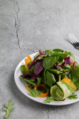 Salatalıklı diyet yeşil salata ve gri arka planda beyaz bir tabakta havuç. Yukarıdan minimalizm görünümü biçiminde dikey yönelimli resim ve kopyalama alanı