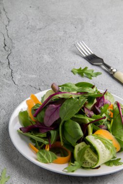 Salatalıklı diyet yeşil salata ve gri arka planda beyaz bir tabakta havuç. Yukarıdan minimalizm görünümü biçiminde dikey yönelimli resim ve kopyalama alanı