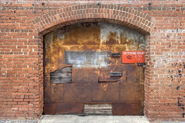 a rusted warehouse delivery receiving bay door and red brick building alley