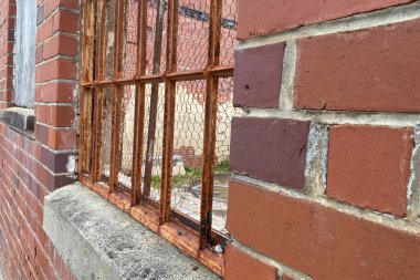 Paslanmış eski parmaklıkların ve tuğla duvarların arasından terk edilmiş bir şantiyeye bakıyorum.