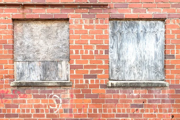 closeup of a red brick wall with boarded up windows