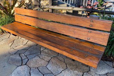 Basit, şık, parlak, süslü, ahşap bahçe bankı. Uzun gölgeli, taş patika bir sokakta.