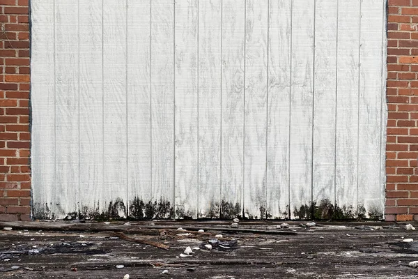 a boarded up white shipping and receiving loading warehouse door in a back alley