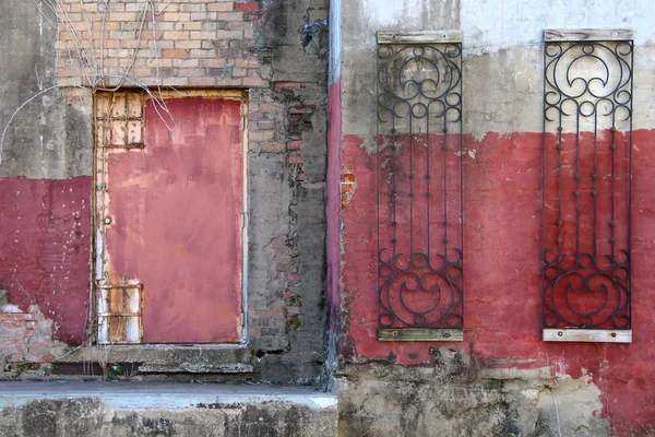 a red fadeing painted dirty warehouse in an alley with red door rusted and concrete steps