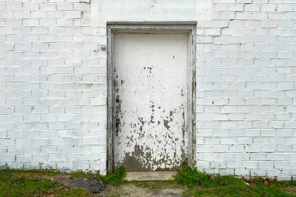 a back alley boarded up doorway with whitewashed brick building in an alley with grass path
