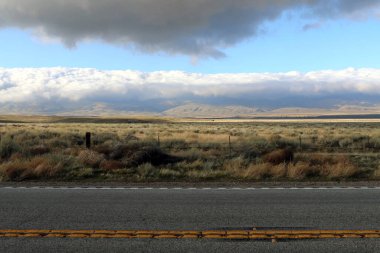 Uzak dağları olan karanlık bir çöl yolu ve gölgeli fırtına bulutları.