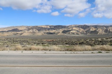 Mavi gökyüzü ve gölgeli bulutları olan bir çöl yolu.