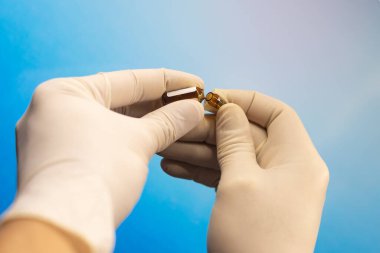 Elleri lastik eldivenlerle yakın plan. Aşıyla açık bir ampul tutuyorlar.