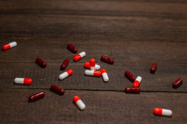 Ahşap arka plana saçılmış kırmızı-beyaz ve kahverengi kapsül hapları. Antibiyotikler