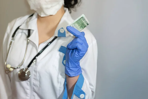 Hundred dollar bill in the hand of a doctor or paramedic. Bribe. Corruption in medicine, pharmaceuticals. The concept of paid medicine.