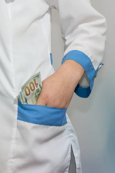 Hundred dollar bill in the pocket of a doctor or paramedic. Corruption in medicine, pharmaceuticals. The concept of paid medicine.