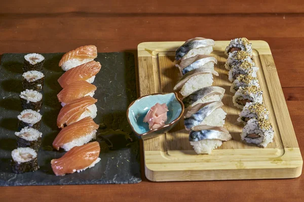 Stock image presentation of various types of fish and rice sushi on table with bowl with ginger and chopsticks