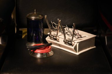 Eski berber aletleri, traş makinesi, makas ve mavi kap, deri malzemelerinin koyu arkaplanda dezenfekte aletleri için