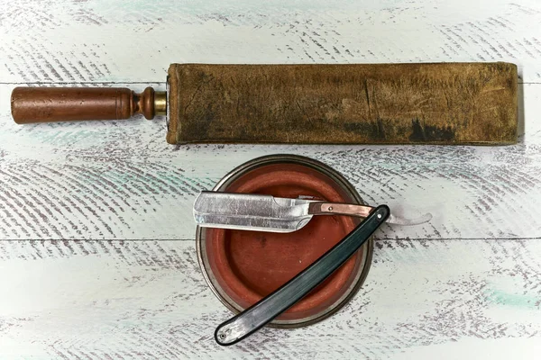 Presentation of old barber tools, a razor with a bowl and a tool for sharpening razors on a white painted wooden background