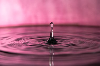 Su damlası pembe arka planda dalgalanmalarla sıçrayan makro