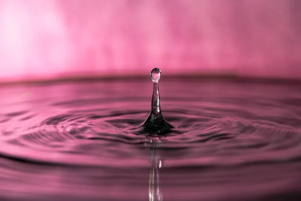 Su damlası pembe arka planda dalgalanmalarla sıçrayan makro