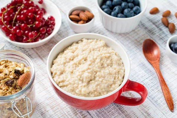 Oatmeal porridge, fresh berries, nuts and granola: healthy breakfast table — Stock Photo, Image