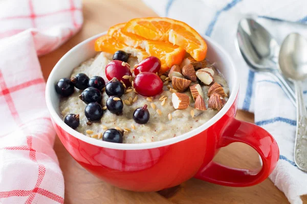 Oatmeal porridge with black currant berries, cranberries, orange slices and almonds — Stock Photo, Image