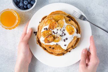 Karamelize muz, yoğurt ve kadın elinde beyaz tabakta çikolata parçaları ile Pancakes