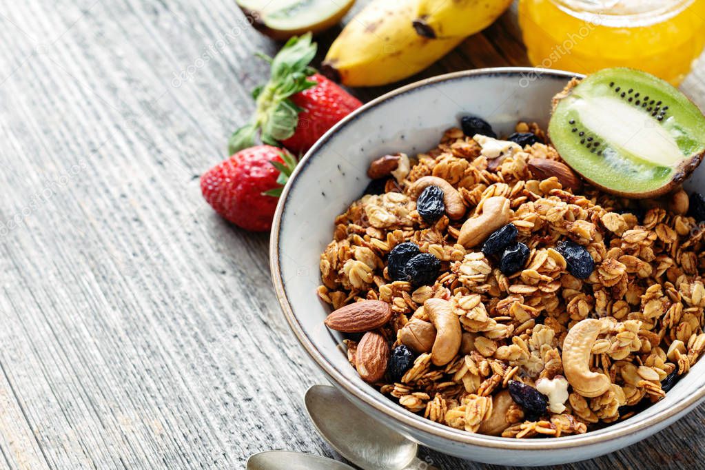 Concept of healthy breakfast food: bowl of granola cereals, fruits and berries on wooden table