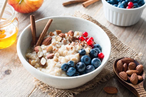 Oatmeal porridge bowl with fruits, nuts and cinnamon in bowl — Stock Photo, Image