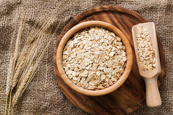 Avena laminada, copos de avena orgánicos en cuenco de madera y espigas de trigo dorado sobre fondo de madera —  Fotos de Stock