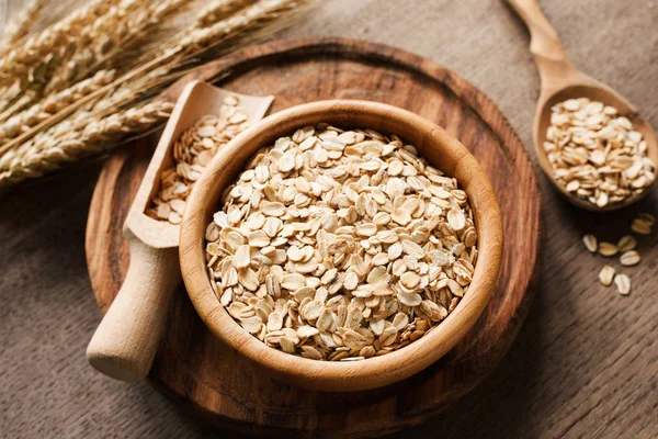 Rolled oats, organic oat flakes in wooden bowl and golden wheat ears on wooden background