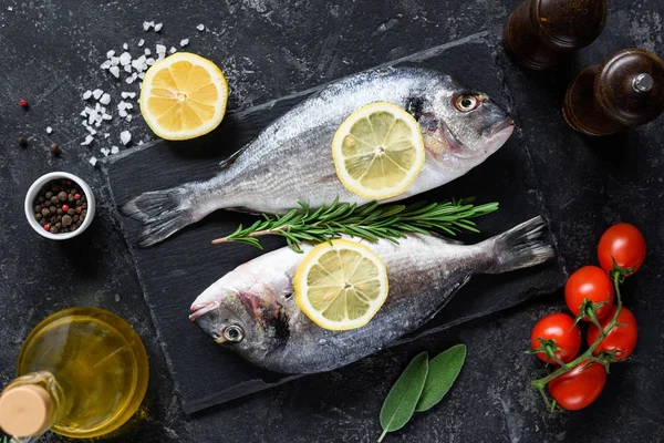 Pescado dorado o besugo fresco sin cocer con rodajas de limón, especias, hierbas y verduras. Comida mediterránea. Vista superior —  Fotos de Stock