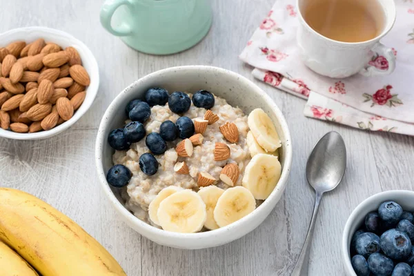 Gesundes Frühstück Haferbrei Schüssel mit Früchten und Nüssen und Tasse grünem Tee — Stockfoto