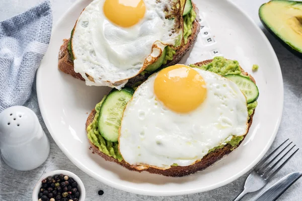Яйцо, авокадо и огуречные тосты на белой тарелке — стоковое фото