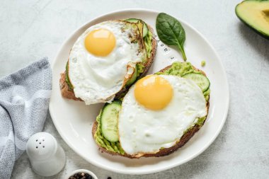 Kahvaltı tost kızarmış yumurta, avokado ve salatalık ile bütün tahıl ekmeği beyaz plaka üzerinde