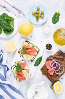 Tost sandviç somon, krem peynir, zeytin ve beyaz masada salatalık ile