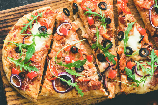 Homemade flatbread pizza with tomato sauce, black olives, onion, mozzarella cheese and fresh arugula on wooden cutting board, top view, toned image