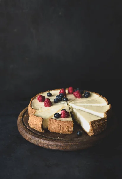 Tarta de queso con bayas frescas en la tabla de cortar sobre fondo oscuro —  Fotos de Stock