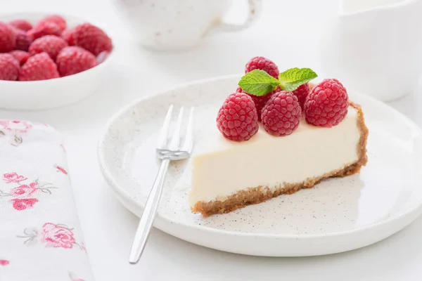 Cheesecake slice with raspberries on white plate