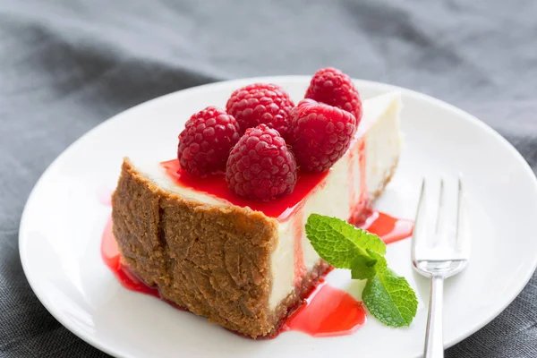 Käsekuchen mit Beerensauce und frischen Himbeeren auf weißem Teller — Stockfoto